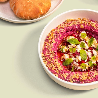 Beetroot dip topped with feta, pomegranate seeds, fresh mint and crushed nuts, served with flatbread on a sage green background