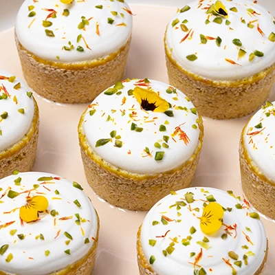 Mini cheesecakes topped with cream, chopped pistachios, saffron threads and yellow edible flowers