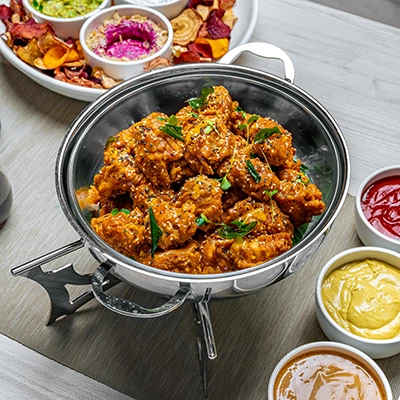 Crispy fried chicken with curry leaves in a serving pan, surrounded by dipping sauces and vegetable crisps